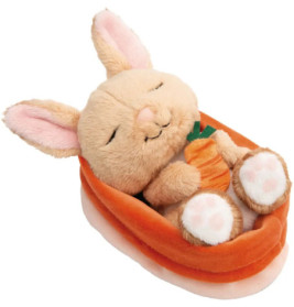 Plüschhase schläft mit Karotte in orange-weißer Bettdecke.