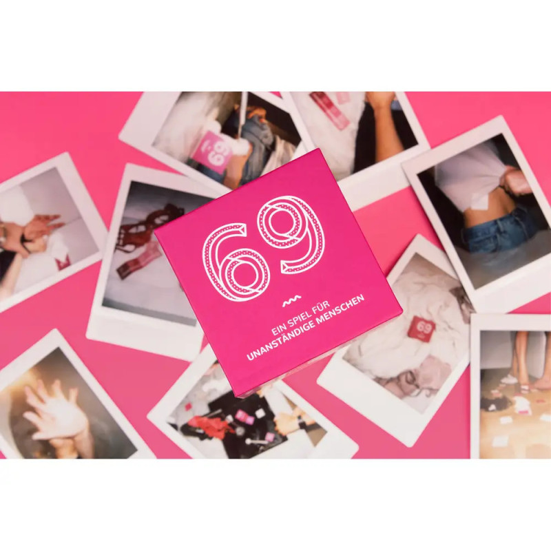 Rosa Kartenspielbox mit der Aufschrift 69 liegt auf verstreuten Sofortbildern vor pinkem Hintergrund.