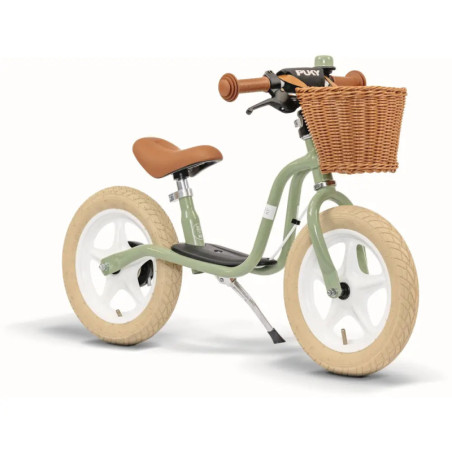 Grünes Laufrad mit weißen Rädern, braunem Ledersitz und Lenker sowie einem vorderen Weidenkorb.