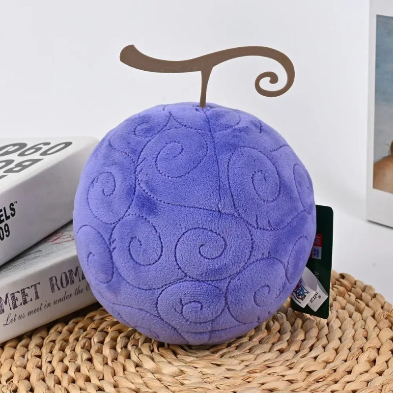 Rundes, lilafarbenes Plüschtier mit Wirbelmuster und braunem Stiel auf geflochtener Matte.