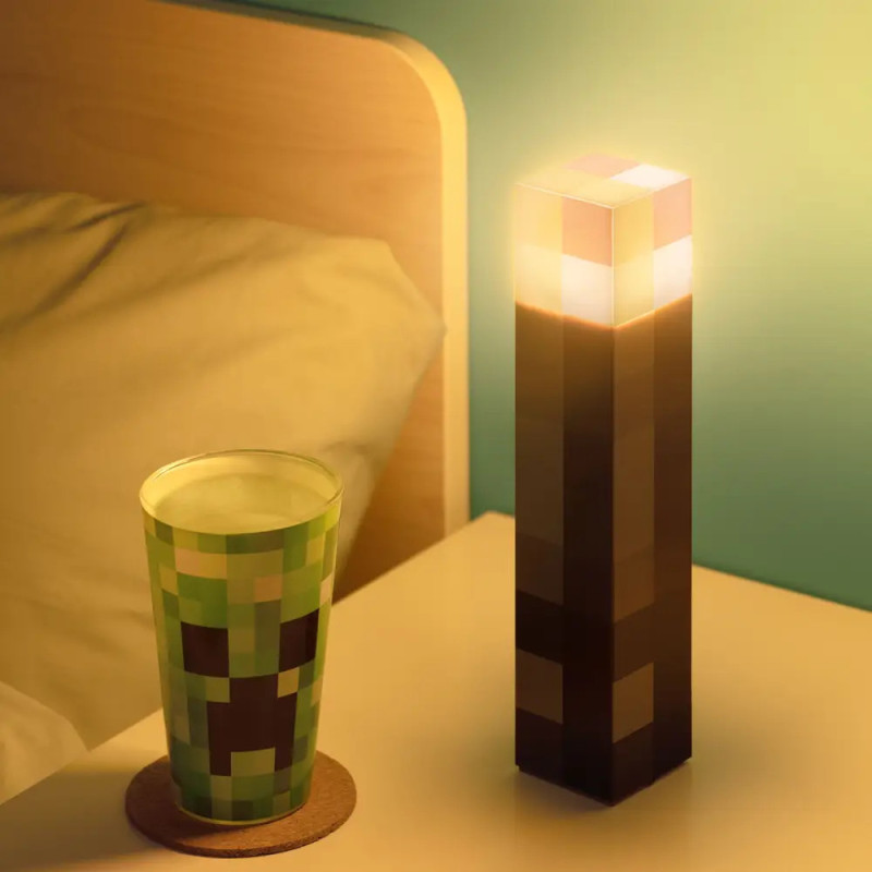 Minecraft-Taschenlampe und Creeper-Becher auf einem Nachttisch neben einem Bett mit Holz-Kopfteil.