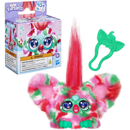 Bunter Furby mit großen Ohren, pinkem Haar und grünem Zubehör neben der Verpackung.