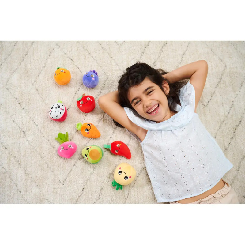 Lächelndes Mädchen liegt auf dem Teppich neben Plüschtieren in Obst- und Gemüseform.