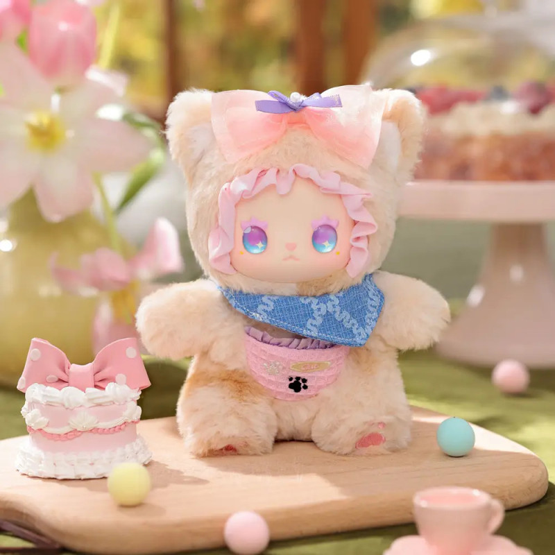 Plüschfigur mit pastellfarbener Schleife und Lätzchen steht auf Tisch neben Kuchen, Blumen und Deko.