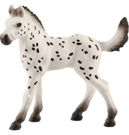 Weiße Fohlenfigur mit schwarzen Flecken, schwarz abgesetzten Ohren, Hufen und Schweif steht auf allen vier Beinen.